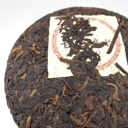 Close-up of a round black tea cake with a white label featuring red text and design.