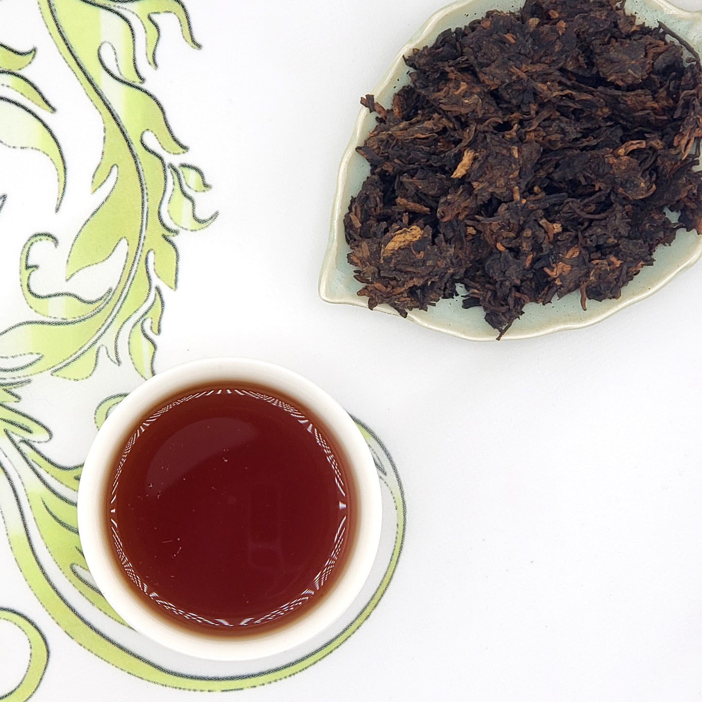 Tea leaves on a plate and a cup of tea on a decorative mat