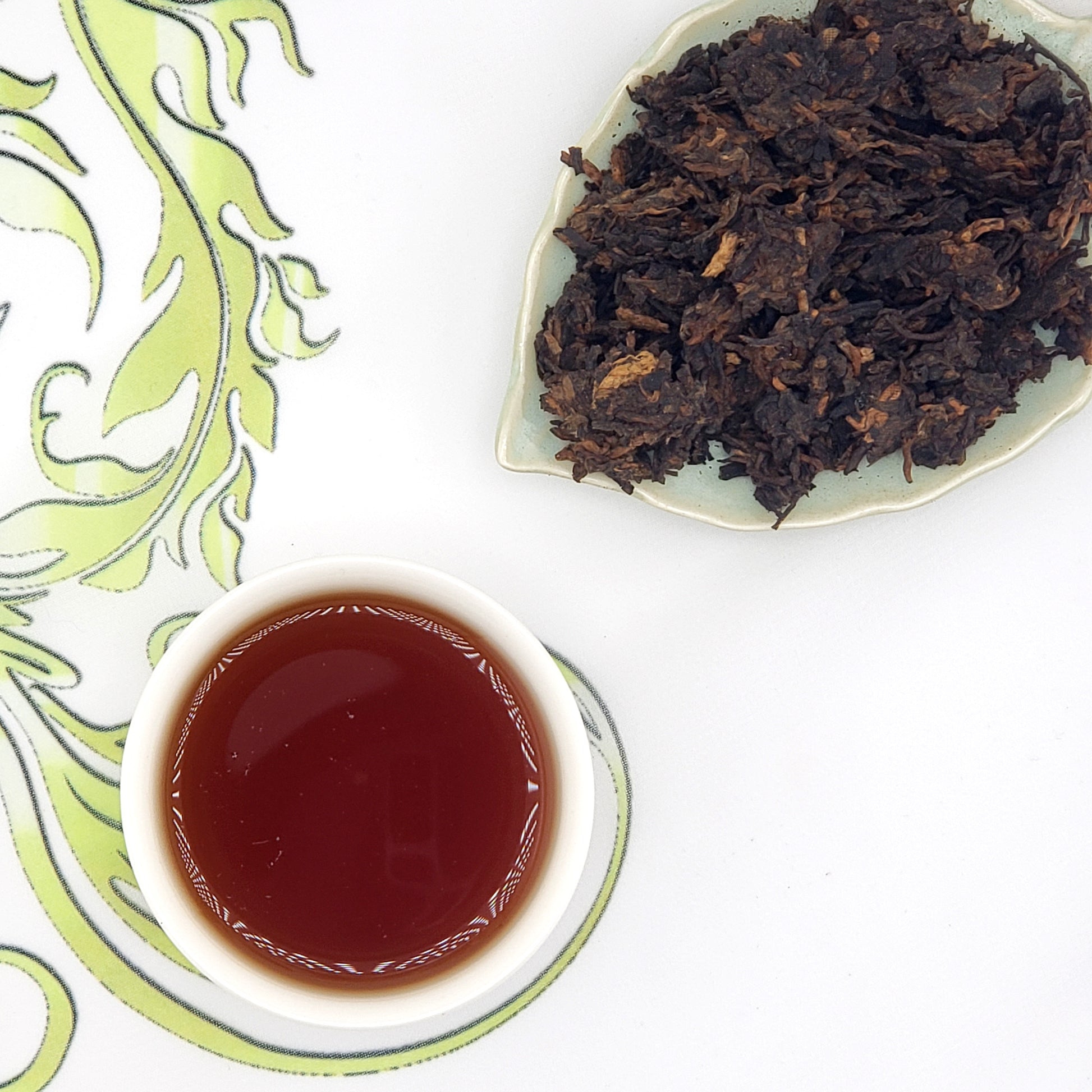 Tea leaves on a plate and a cup of tea on a decorative mat