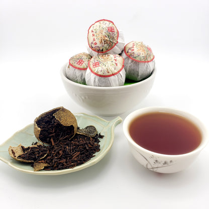 Tea leaves, a bowl of wrapped tea balls and a cup of tea on a white background