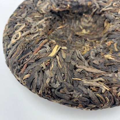 Close-up of a compressed tea cake with dark brown and gold leaves on a white background