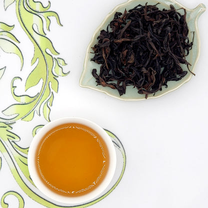 Dried oolong tea leaves on a leaf-shaped dish with a cup of brewed tea.