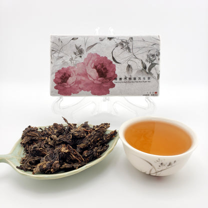Tea brick with floral design, a cup of tea, and a spoonful of tea leaves on a white background