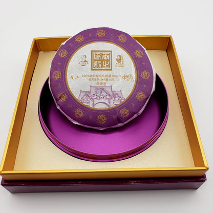 Small cake of Pu-erh tea with decorative purple and gold wrapper inside purple and gold gift box.