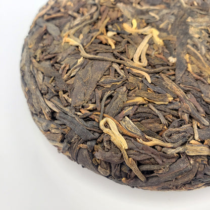 Close-up of a compressed tea cake with dried tea leaves on a white background