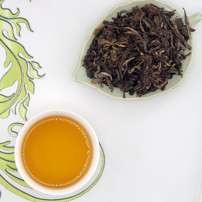 Dried tea leaves on a leaf-shaped plate with a cup of brewed tea on a white background