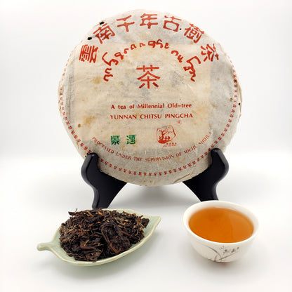 Pu-erh tea cake with a scoop of tea leaves and a cup of tea on a white background