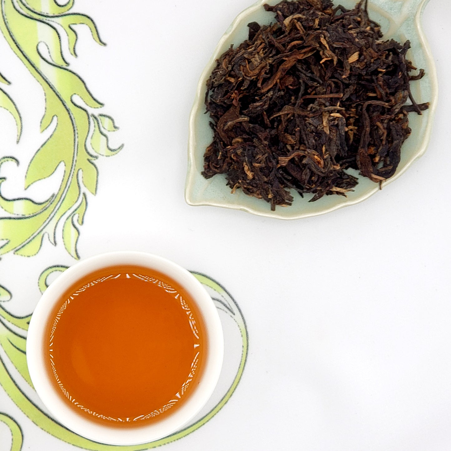 Dried tea leaves on a leaf-shaped dish with a cup of brewed tea.