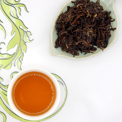 Dried tea leaves on a leaf-shaped dish with a cup of brewed tea.