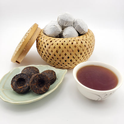 Tea leaves in a woven container, tea balls on a plate, and a cup of tea on a white background