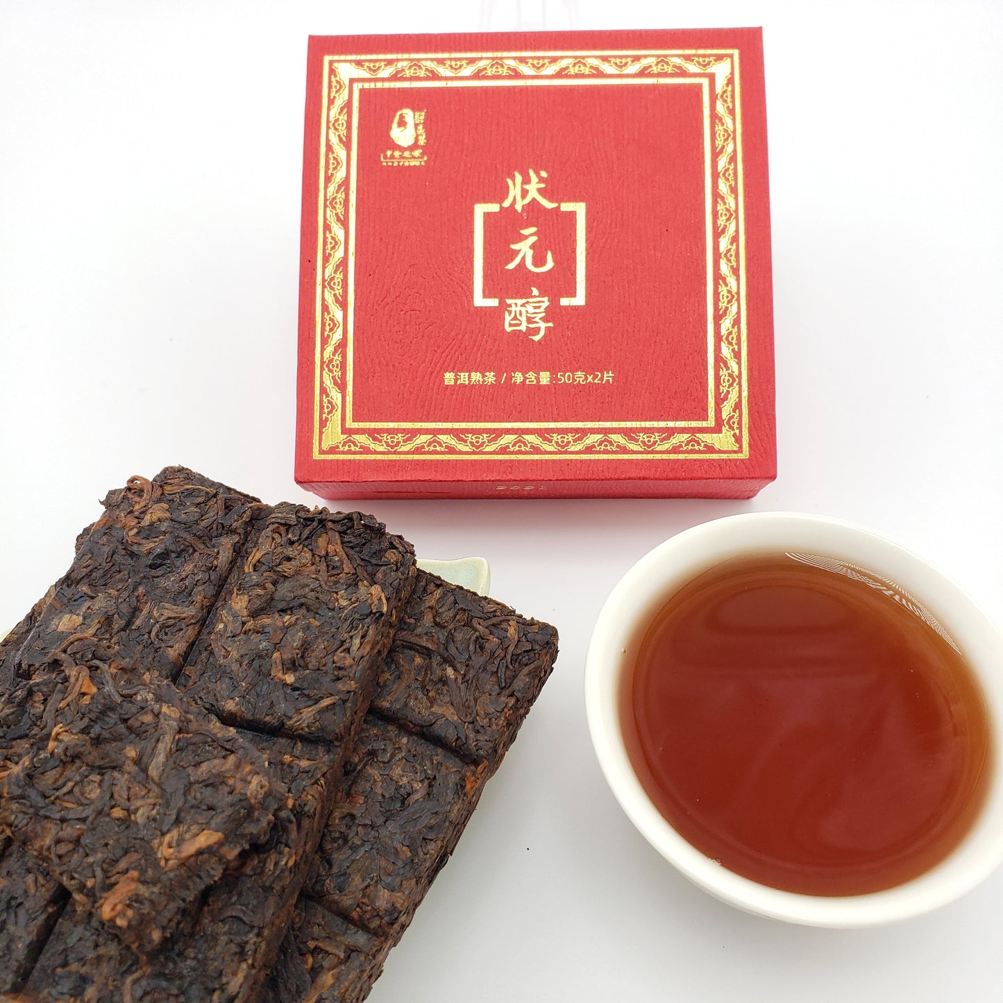 Red tea box, white cup with tea, and dark tea bricks on a white background