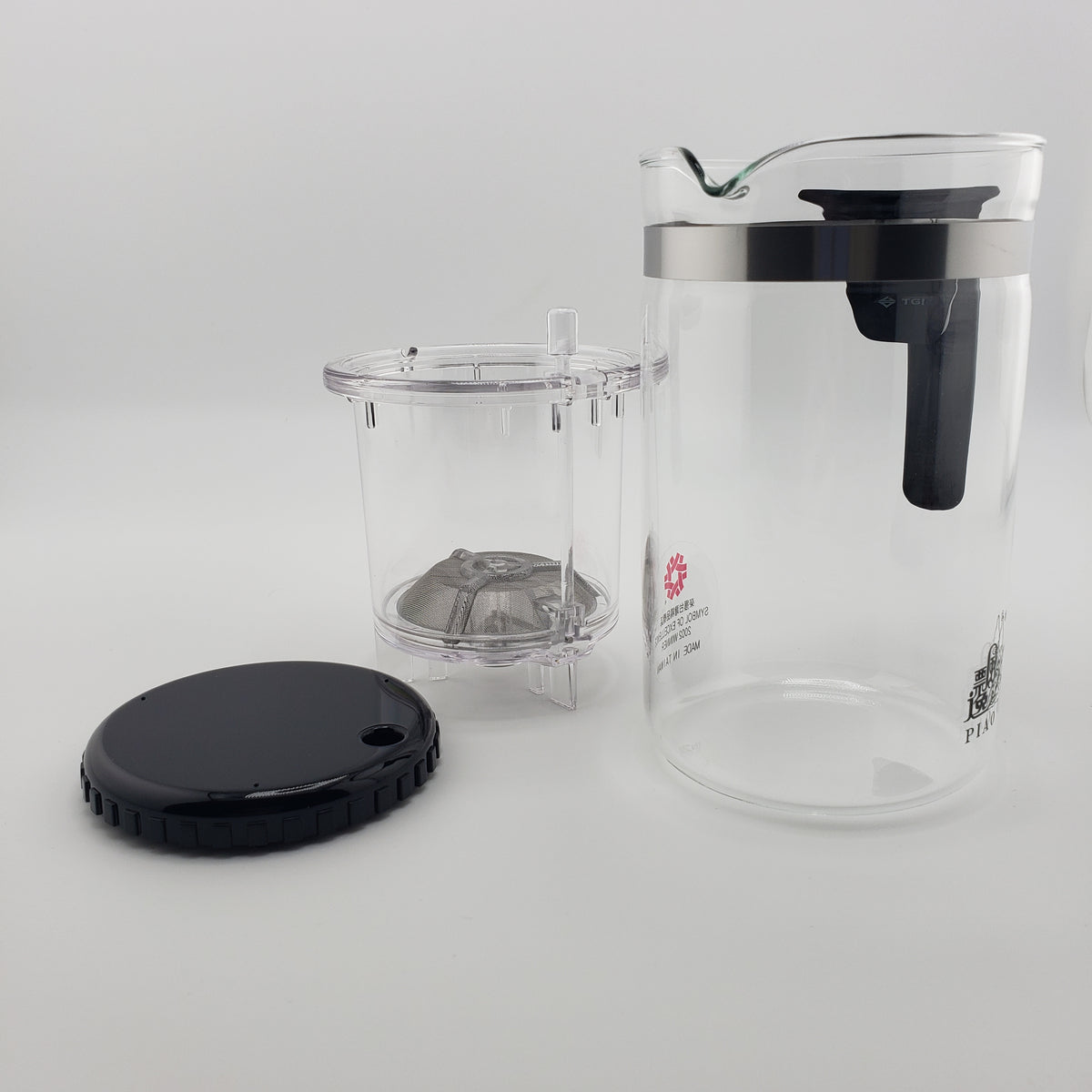 A clear glass teapot with a black lid and handle, shown with its clear infuser basket and black lid on a light gray background.
