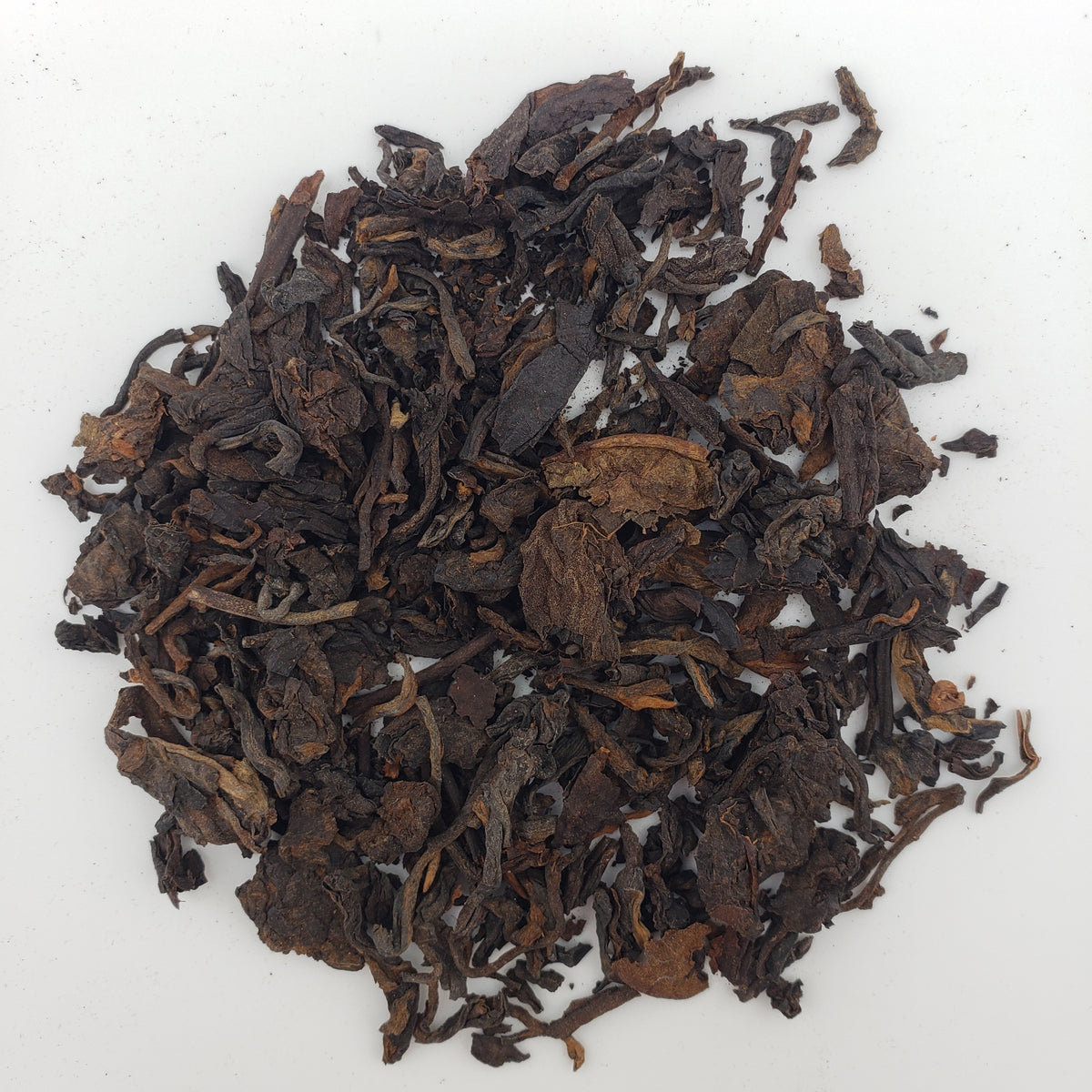 Close up of dark brown Pu-erh tea leaves on a white surface.