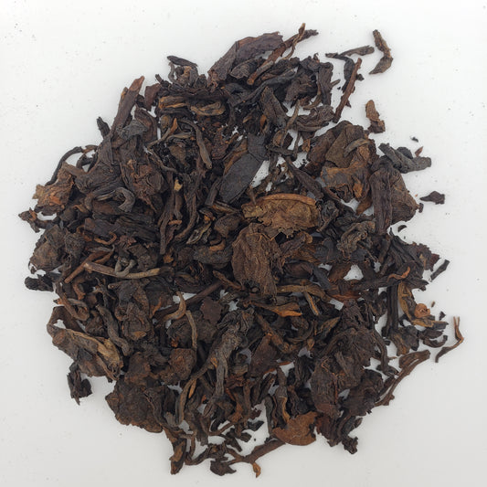 Close up of dark brown Pu-erh tea leaves on a white surface.