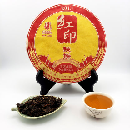 Tea cake with a yellow and red label, a cup of tea, and a scoop of tea leaves on a white background.