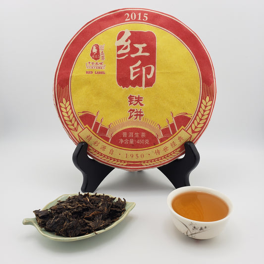 Tea cake with a yellow and red label, a cup of tea, and a scoop of tea leaves on a white background.