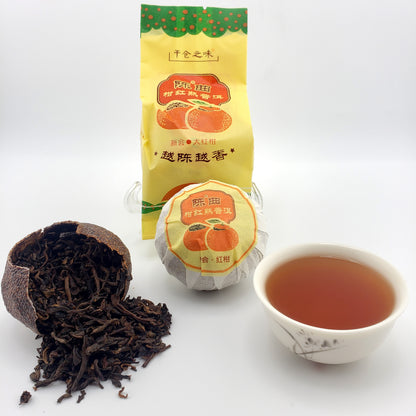 Tea packaging, cup of tea, and tea leaves spilling out of a broken dried red mandarin shell on a white background