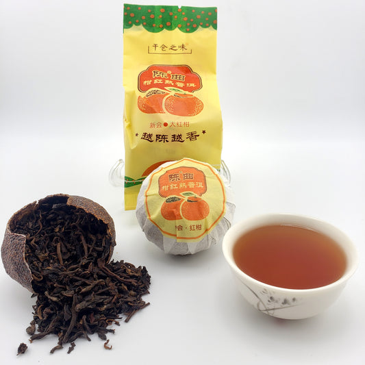 Tea packaging, cup of tea, and tea leaves spilling out of a broken dried red mandarin shell on a white background