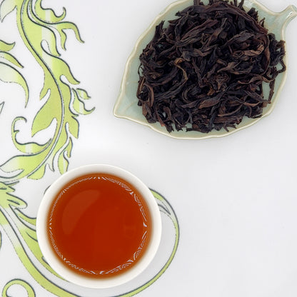 Dried oolong tea leaves on a leaf-shaped plate with a cup of brewed tea on a decorative white background.