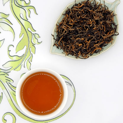 Dried tea leaves on a leaf-shaped dish with a cup of brewed tea on a decorative white background.