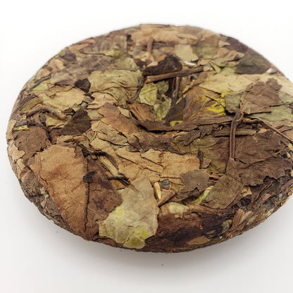 Round compressed tea cake with dried leaves on a white background