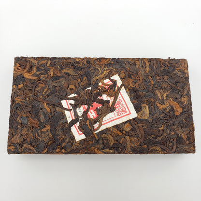 Rectangular block of dark brown tea leaves with a red and white label on a white background