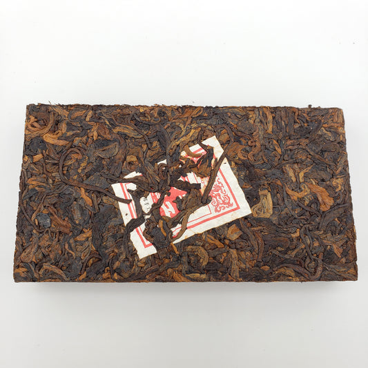 Rectangular block of dark brown tea leaves with a red and white label on a white background