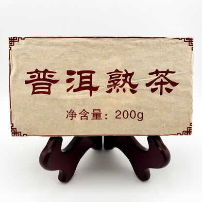 Tea brick with white and red packaging. Text reads "200 g" and Chinese text states "Pu-erh ripe tea"