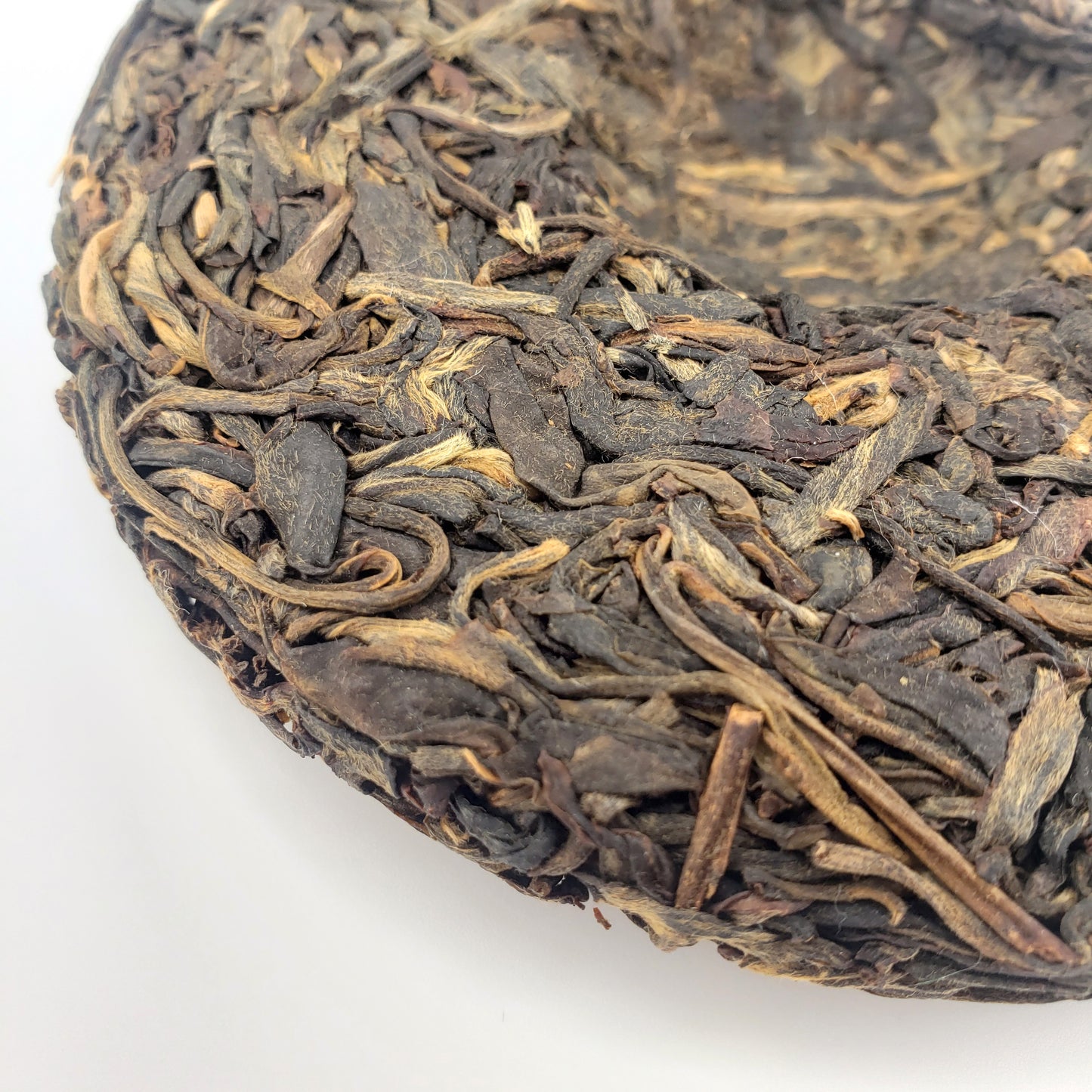 Close-up of a compressed tea cake with dried tea leaves on a white background