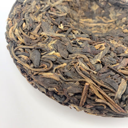 Close-up of a compressed tea cake with dried tea leaves on a white background