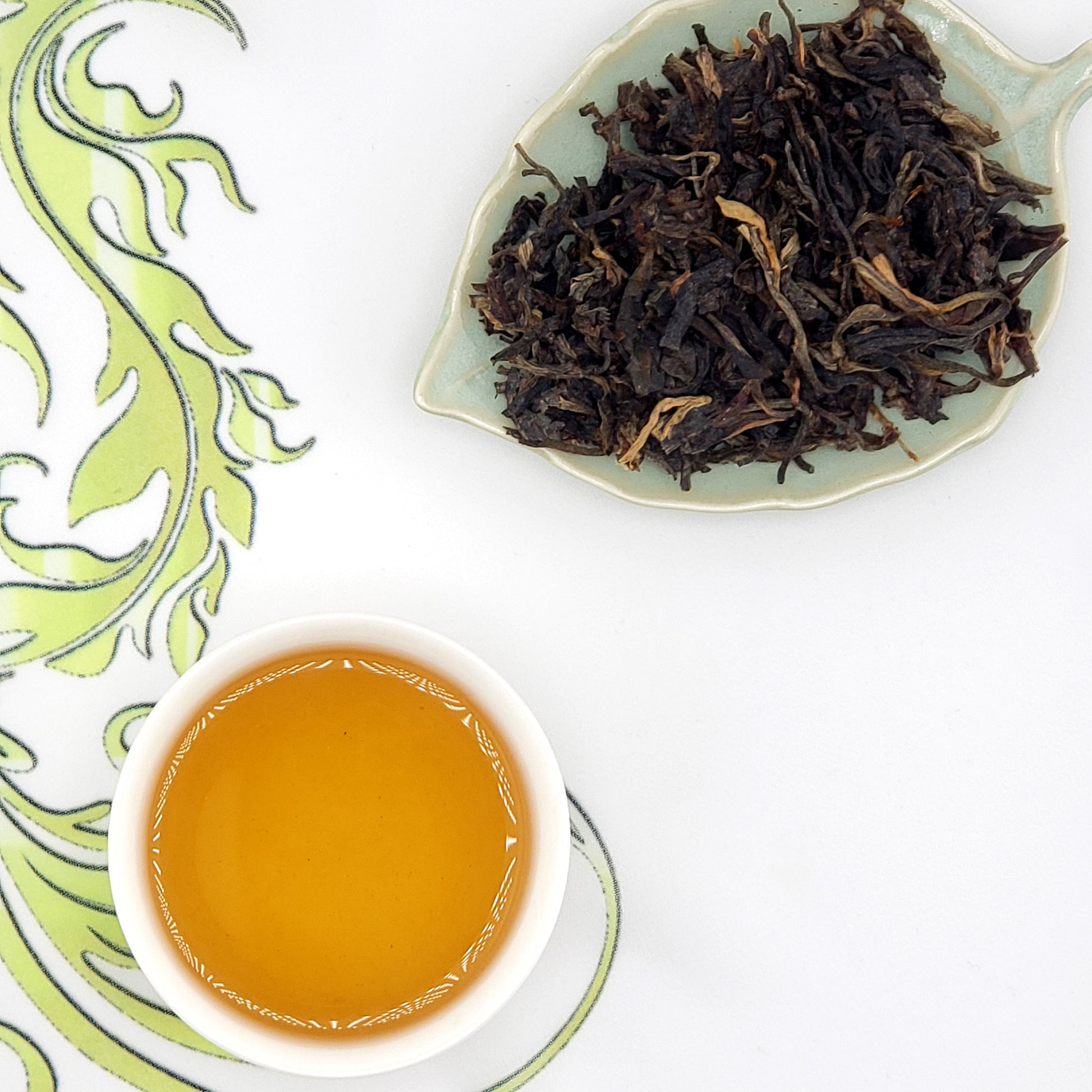 Tea cup with brewed tea and a dish of dry tea leaves on a decorative white background