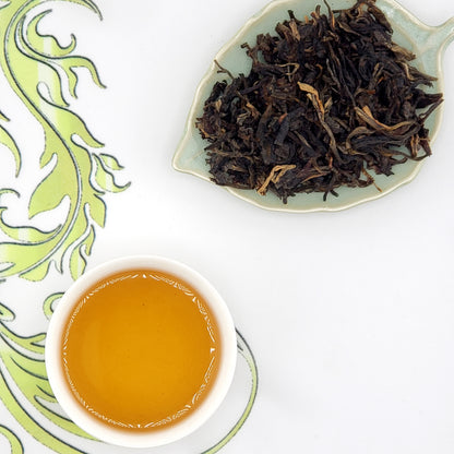 Tea cup with brewed tea and a dish of dry tea leaves on a decorative white background