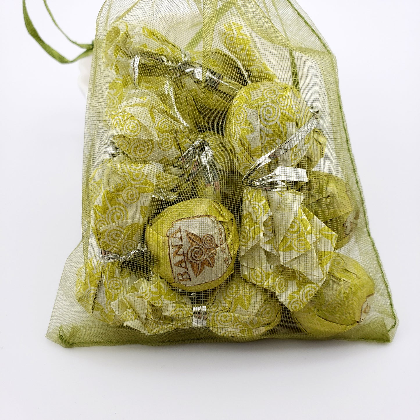 Green mesh bag filled with wrapped tea balls on a white background