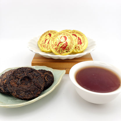 Tea leaves, a cup of tea, and gold-wrapped pressed tea coins on a white surface