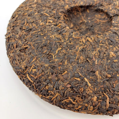 Close-up of a dark brown tea cake with visible tea leaves on a white background