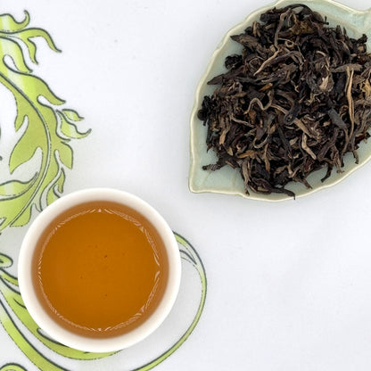 Tea leaves on a leaf-shaped plate with a cup of brewed tea on a white background