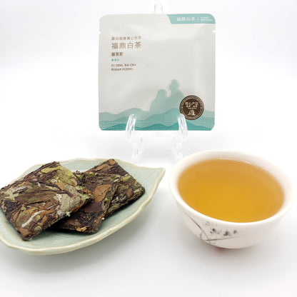 Tea leaves on a plate with a cup of tea and packaging in the background