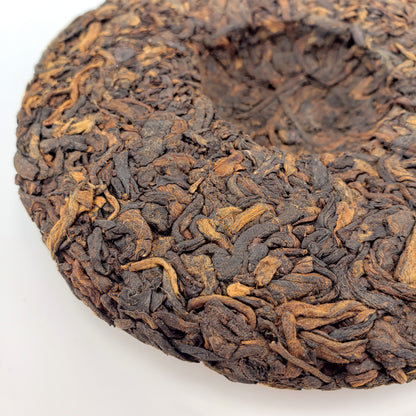 Close-up of a compressed tea cake with dark brown leaves on a white background