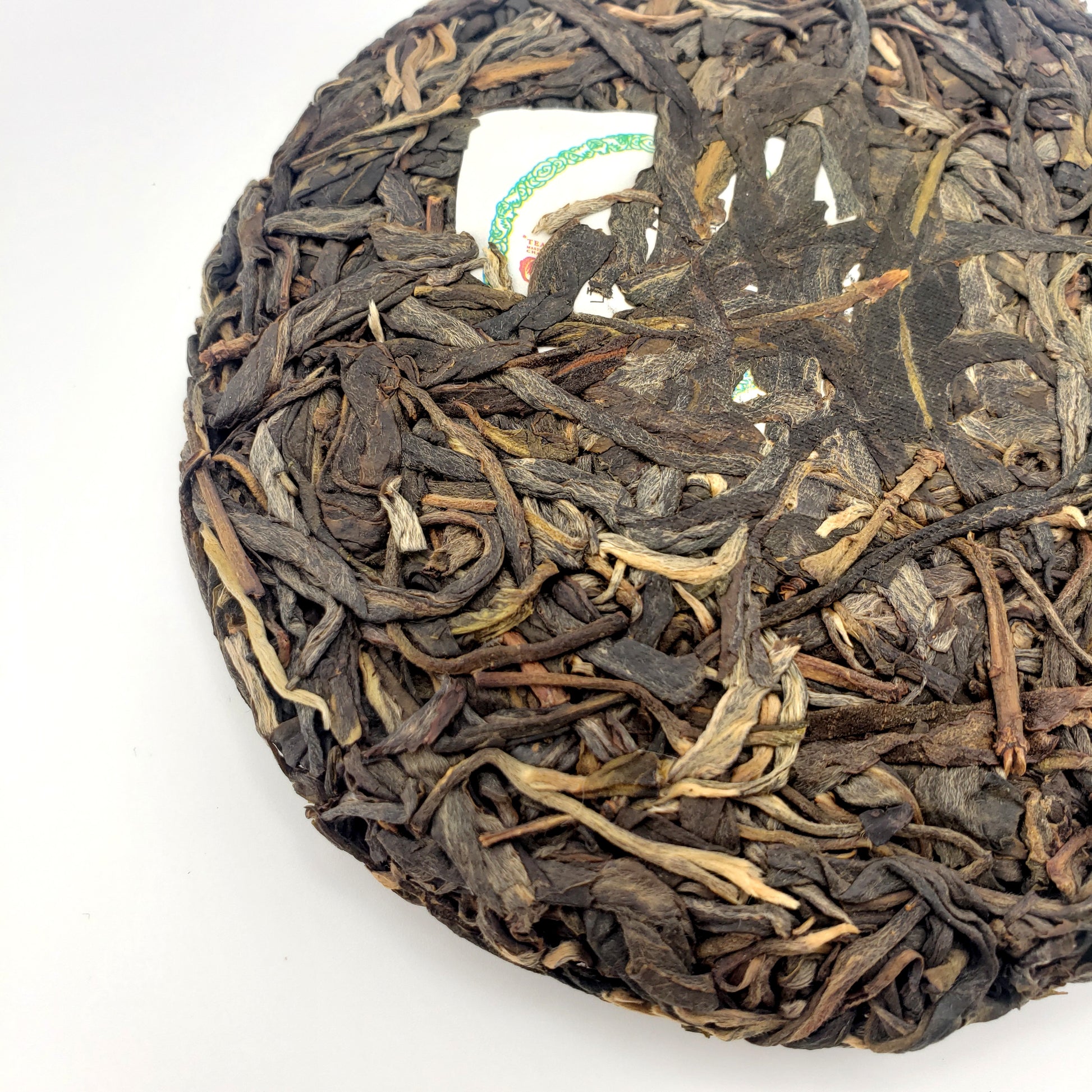 Close-up of a round, pressed tea cake with dried tea leaves on a white background