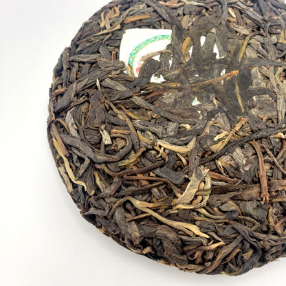 Close-up of a round, pressed tea cake with dried tea leaves on a white background