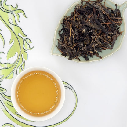 Dry tea leaves on a leaf-shaped dish with a cup of brewed tea on a decorative white background.