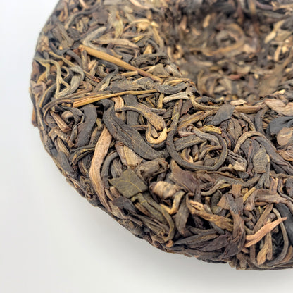 Close-up of a compressed tea cake with twisted tea leaves on a white background