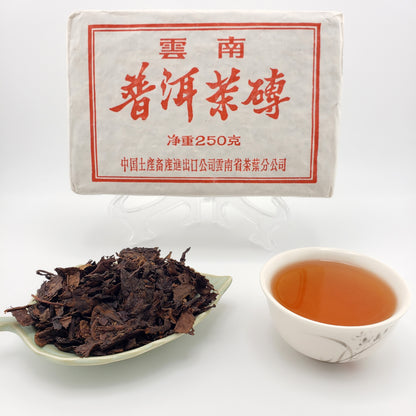 Tea package, tea leaves on a spoon, and a cup of tea on a white background