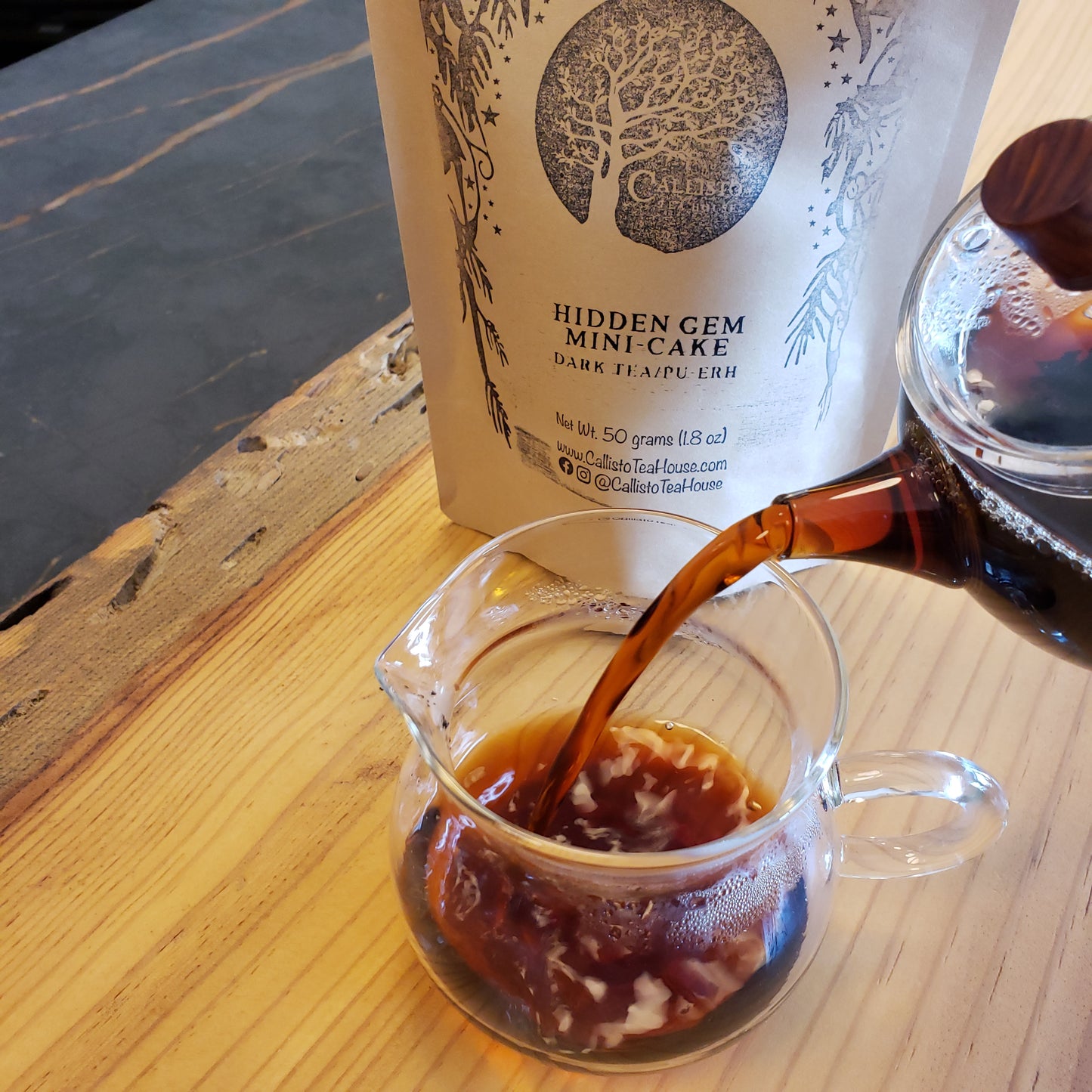 Brewed Pu-erh tea being poured from a glass pot into a pitcher