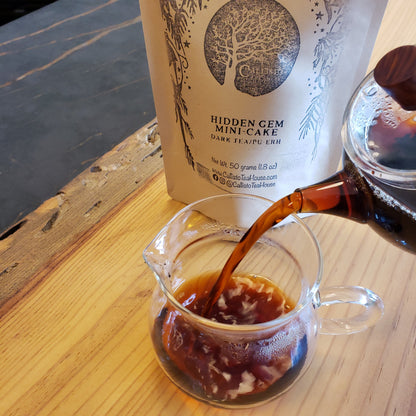 Brewed Pu-erh tea being poured from a glass pot into a pitcher