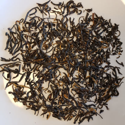 Dried loose-leaf tea leaves, primarily dark brown with lighter golden-brown tips, scattered on a plain white surface.