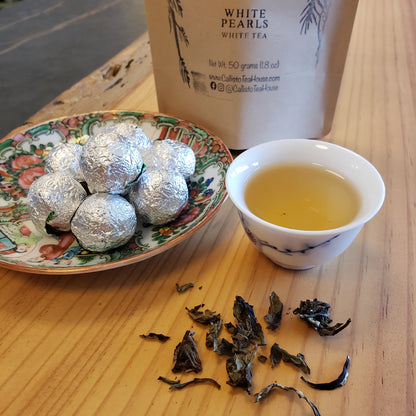 Tea packaging, cup of tea, and dried tea leaves on a wooden surface