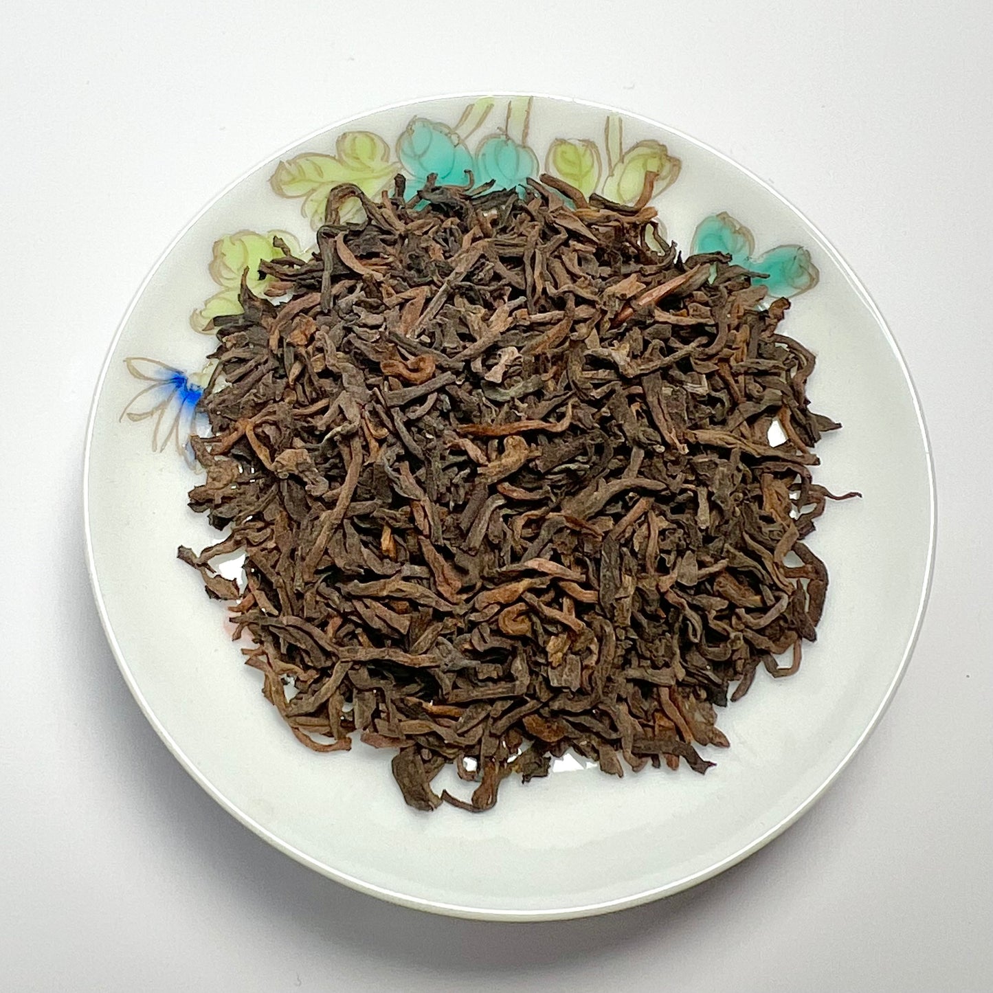 Dried tea leaves on a decorative white plate with floral patterns
