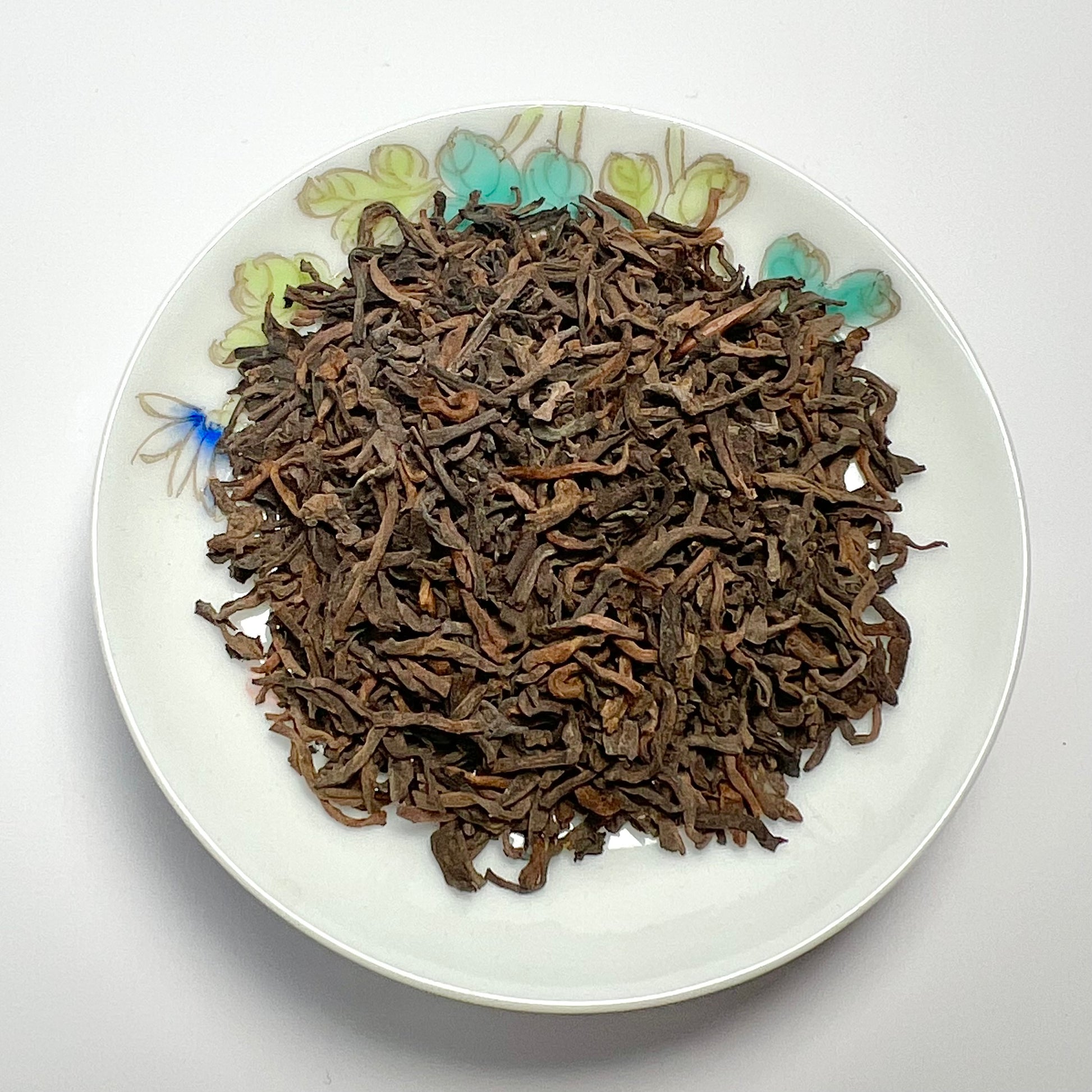 Dried tea leaves on a decorative white plate with floral patterns