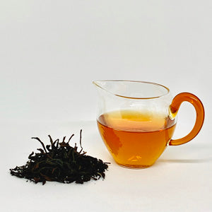Tea leaves and a glass teapot with tea on a white background